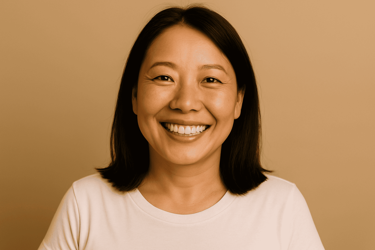 A smiling Asian woman facing the camera with smooth, clear skin on her neck after skin tag removal, against a plain, solid background.