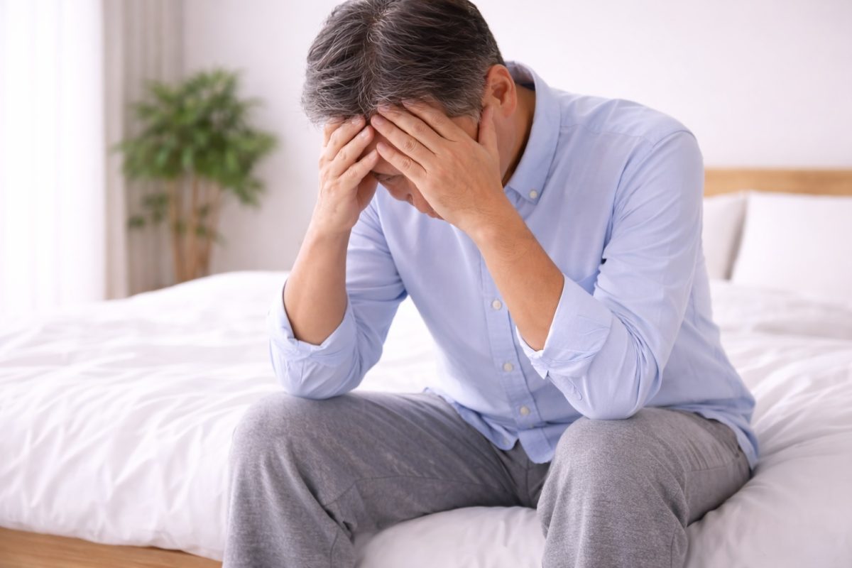 seorang lelaki duduk di atas katil sambil memegang kepalanya