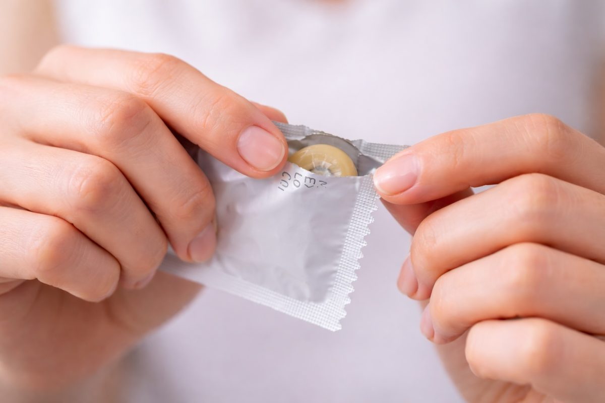 Person opening condom wrapper, highlighting protection methods for preventing STDs during sexual activity