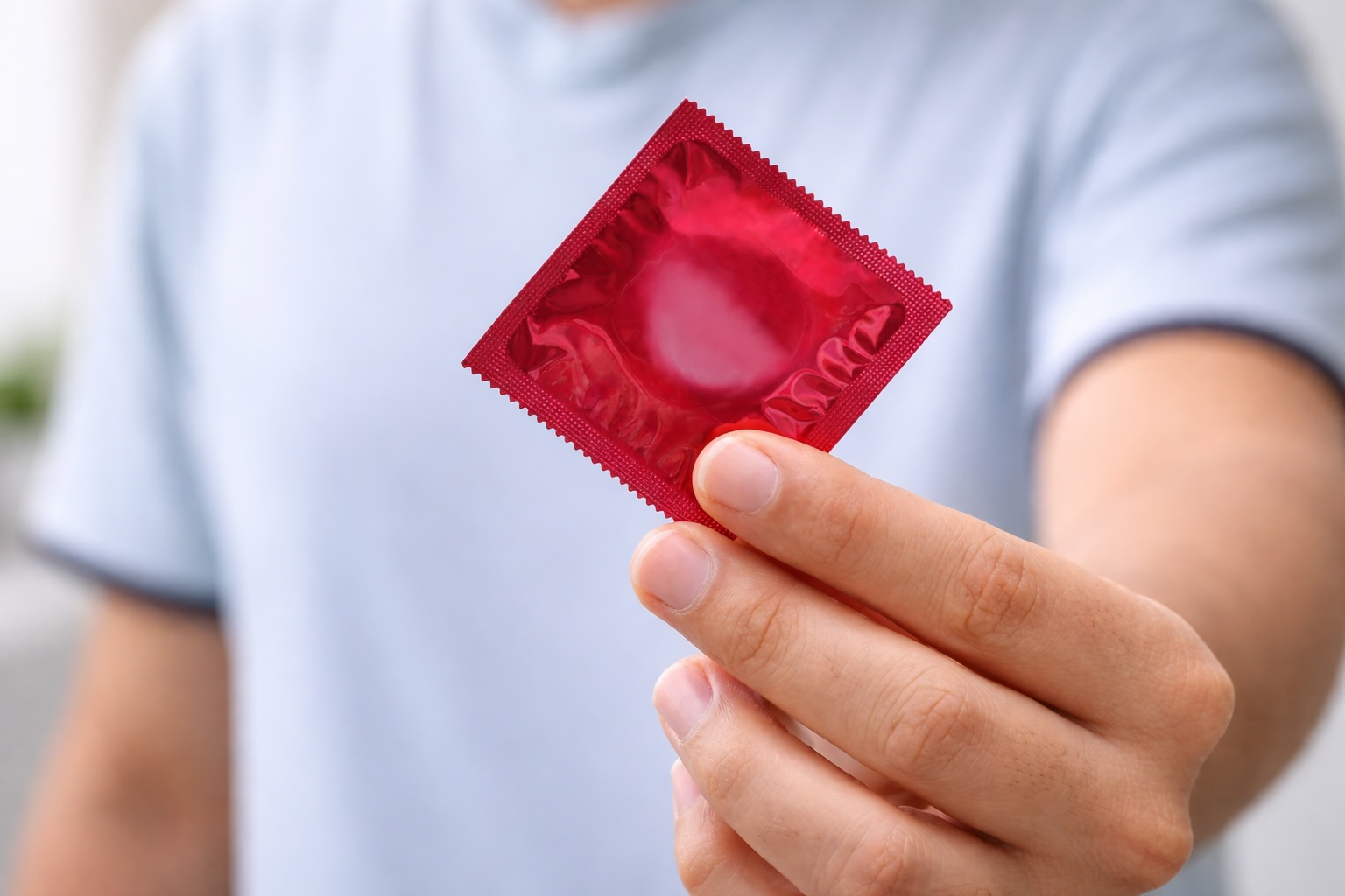 Person holding a condom wrapper, highlighting safe sex practices to reduce the risk of STDs and STIs