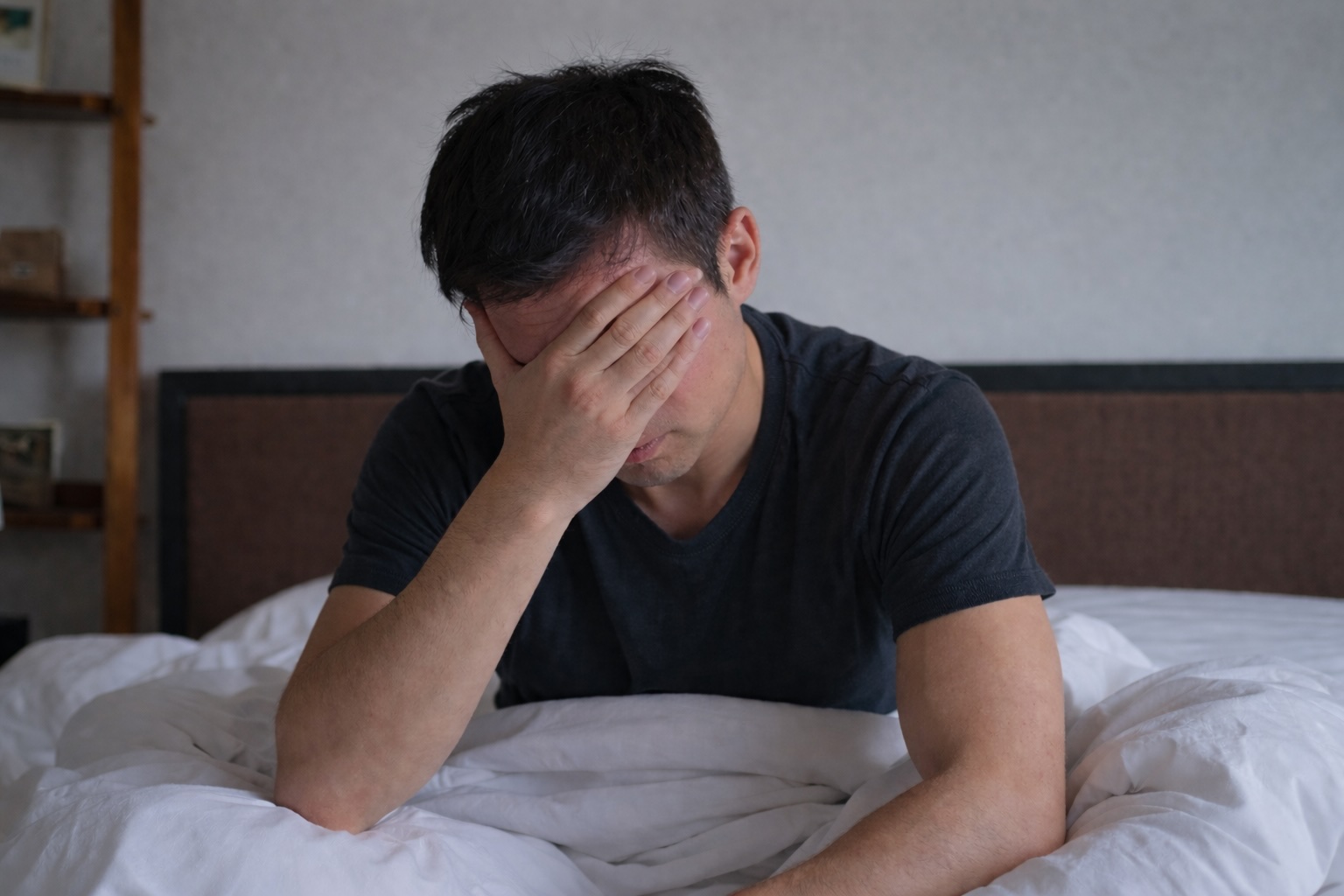 Man sitting on bed with hand on face, showing stress or discomfort linked to painful ejaculation or sexual health concerns