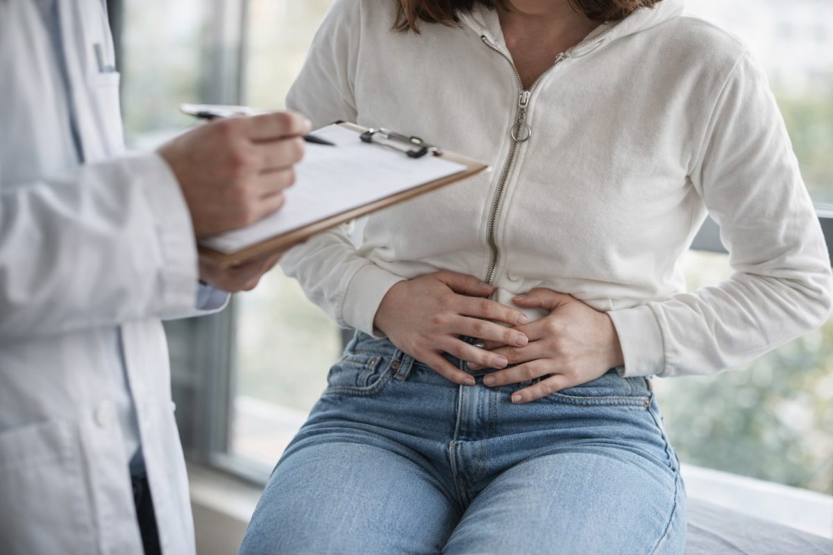 Woman holding lower abdomen in pain while consulting a doctor, illustrating pelvic inflammatory disease symptoms and discomfort