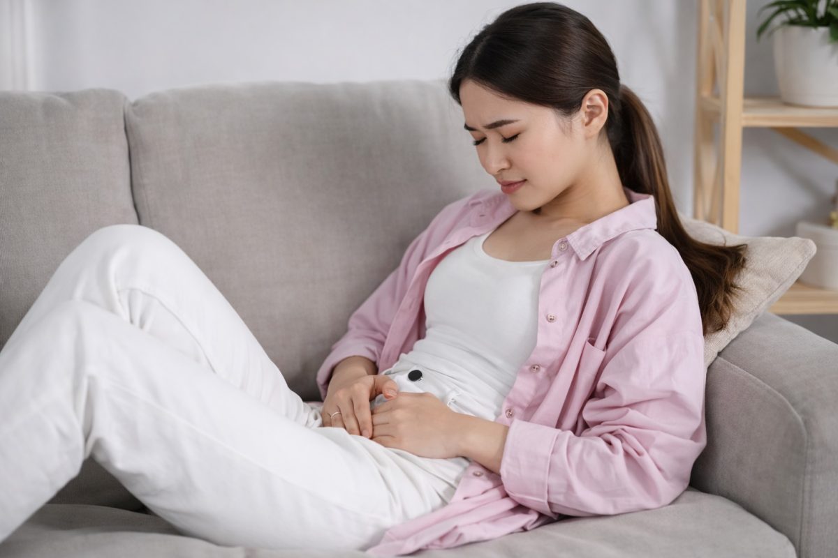 Woman resting on sofa with lower abdominal discomfort, representing recurring UTI symptoms or pelvic pain concerns