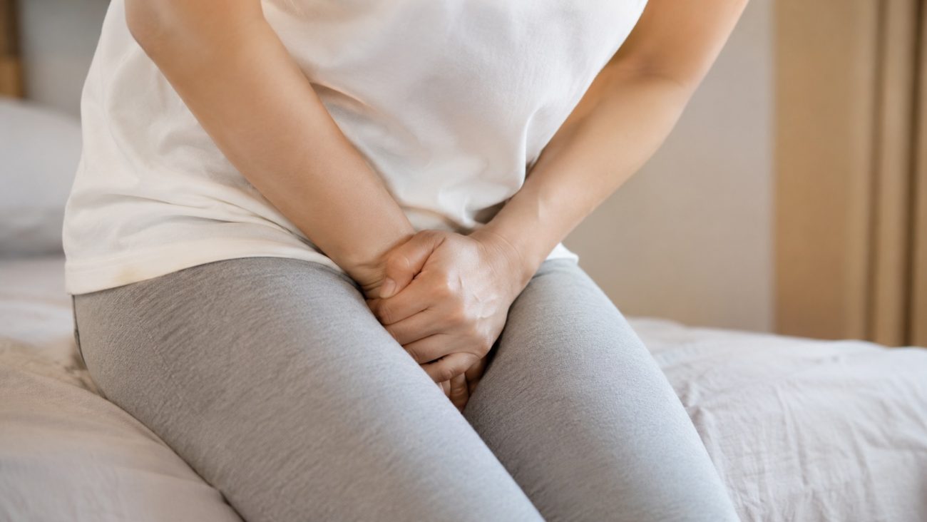 Woman experiencing pelvic discomfort and possible std symptoms while sitting on a bed at home.