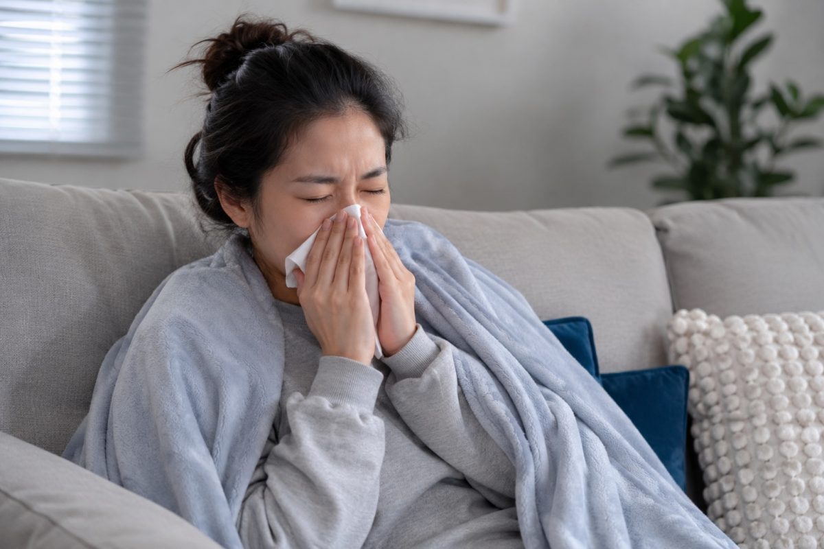 Woman with flu-like symptoms sneezing into a tissue, a possible sign associated with infection or illness