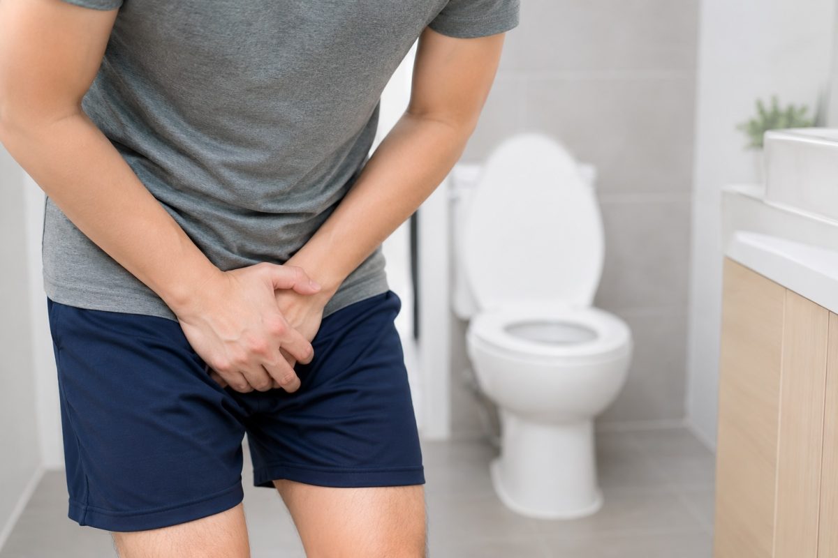 Man experiencing groin discomfort near the toilet, representing possible urinary or testicular pain symptoms.